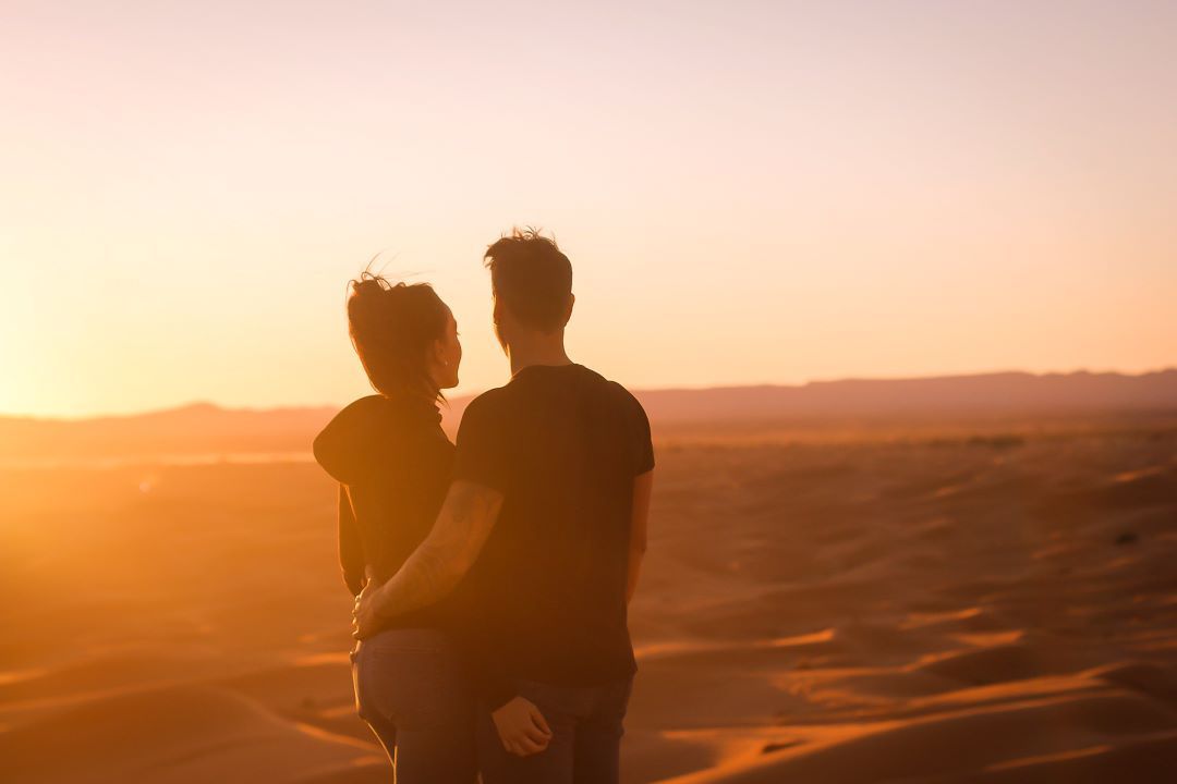 pareja al atardecer cogidos de la cintura mirando al horizonte al atardecer en el desierto en marruecos